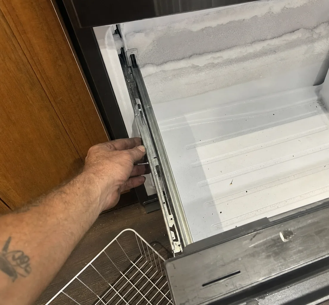 A freezer drawer pulled open on its runners, a ridge of frost banked along the top of the compartment behind it.