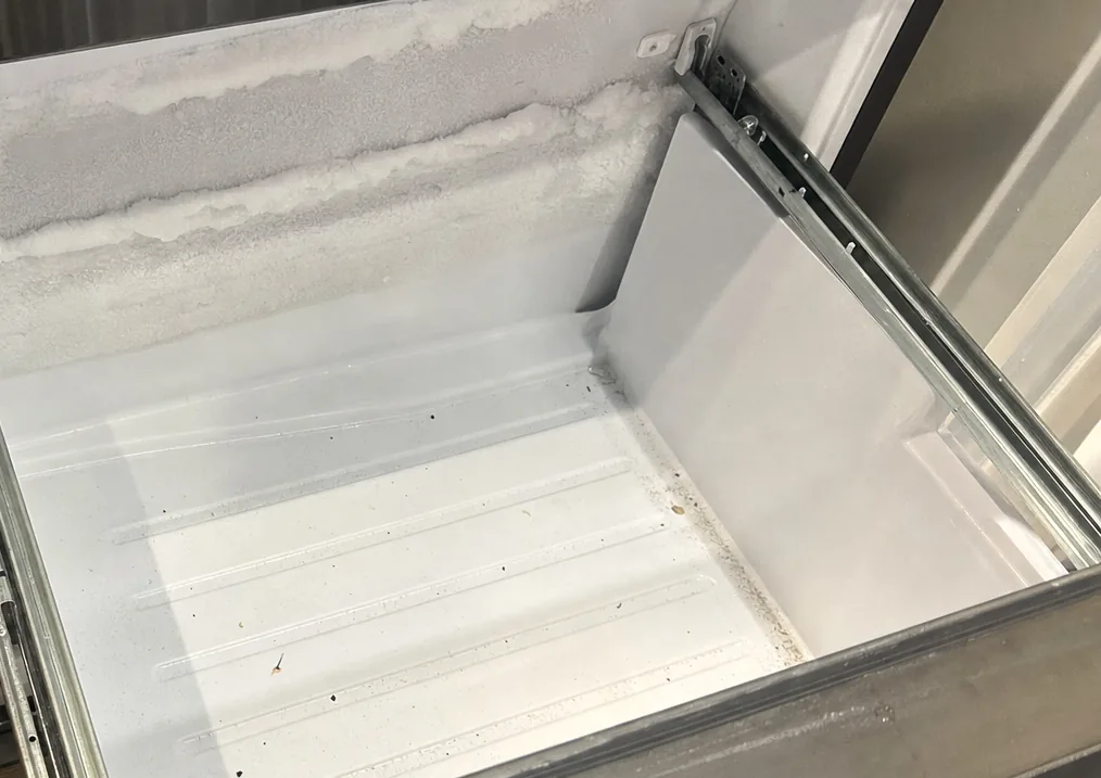 The interior of a freezer drawer photographed from above, frost across the back wall and the drawer rails at the edge of frame.